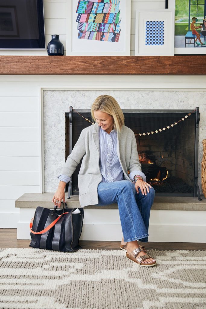 Melissa Mahoney sits in front of her living room marble fireplace. Her fireplace mantle is adorned with colorful artwork she has collected over the years. She is passionate about helping homeowners transform their house into their thoughtfully designed home.