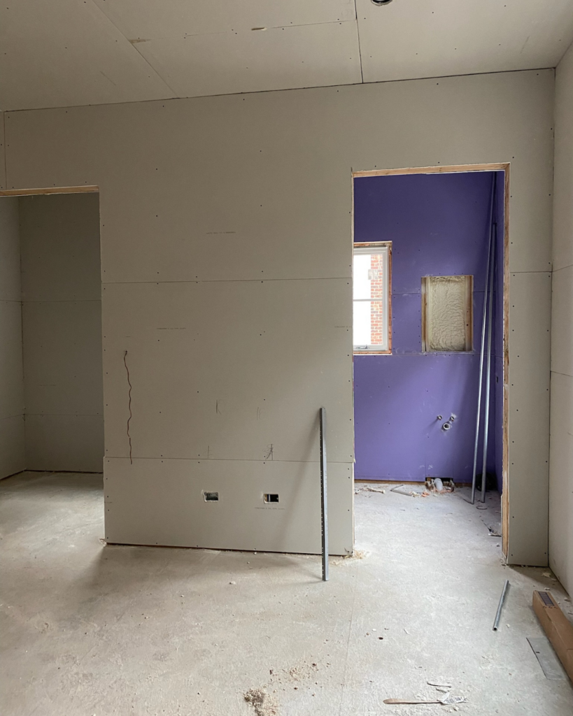 Initial phase of guest bathroom construction viewed from guest bedroom, showing newly installed drywall.