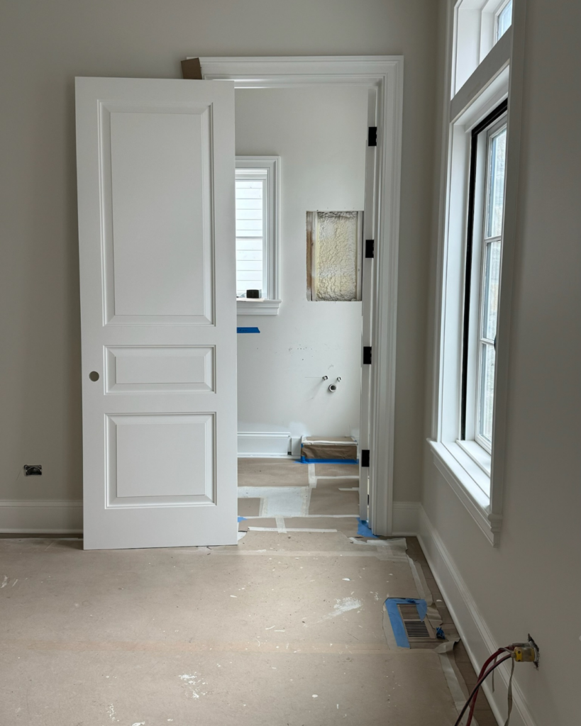 Guest bathroom construction phase with installed moldings and doors, viewed from guest bedroom.