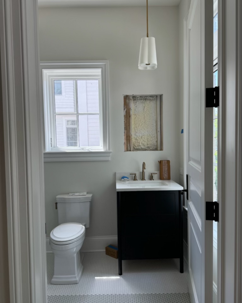 Progress phase of guest bathroom with installed vanity, wood flooring, and tile work.