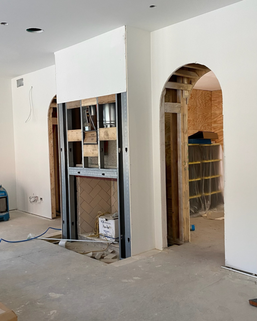 Progress phase of living room transformation showing framed walls with newly installed drywall and ongoing construction details.