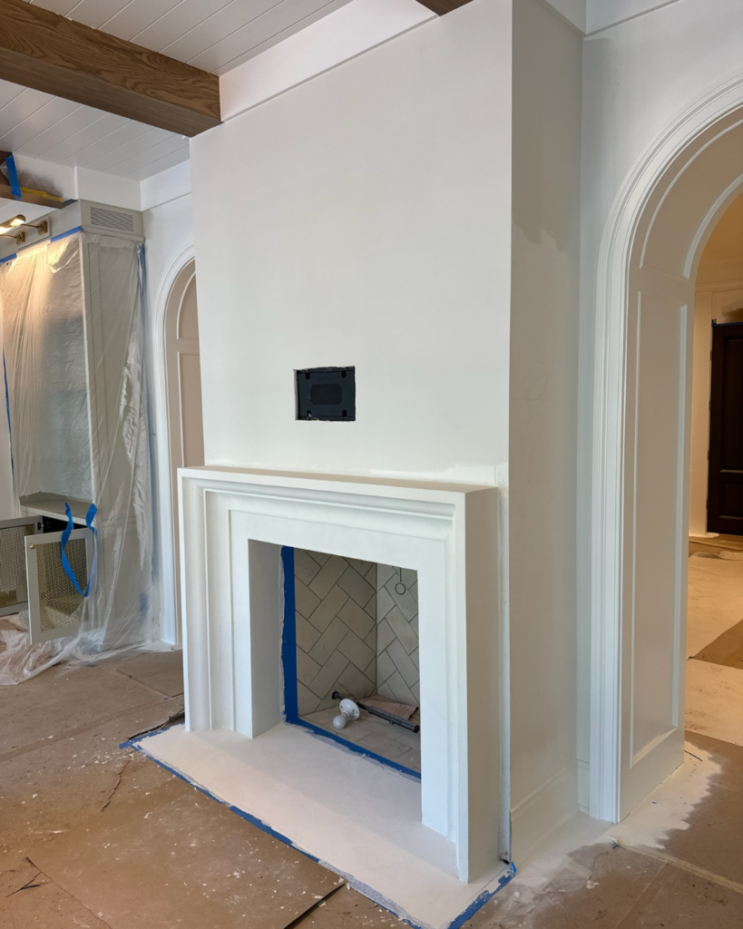 Progress phase of living room transformation showing framed walls, newly installed drywall, and the installation of a plaster fireplace.