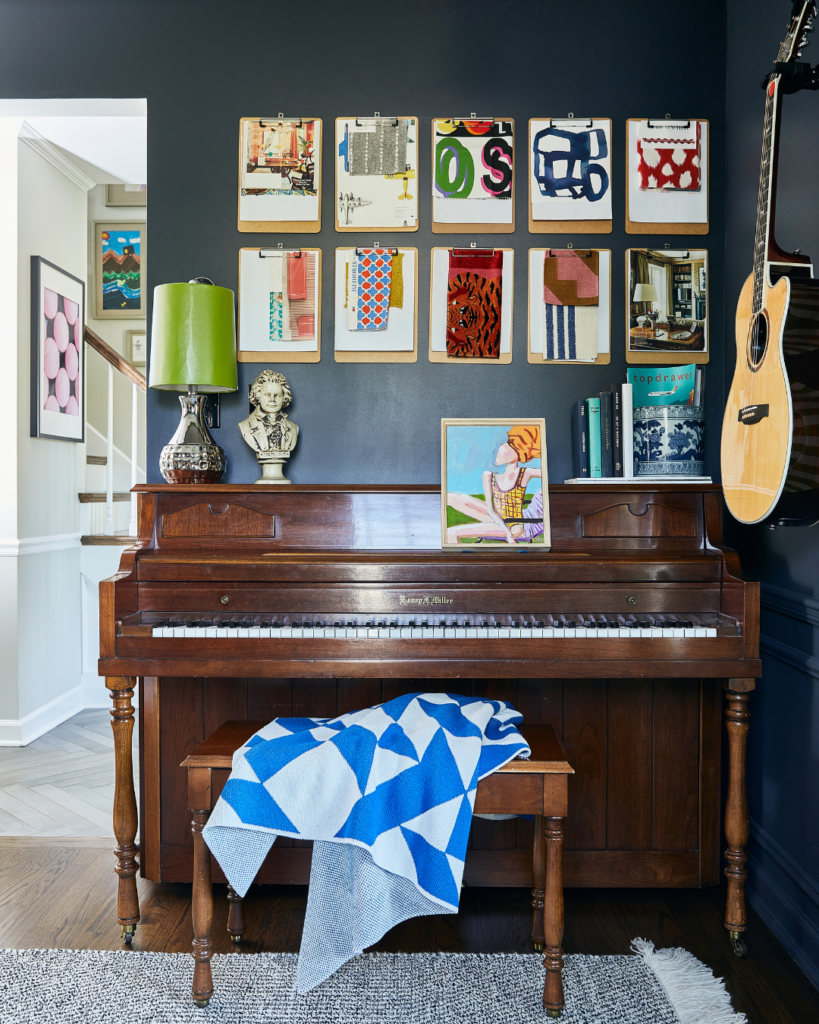 Room with dark navy walls, vibrant artwork, and a piano, highlighting a stylish home refresh project.