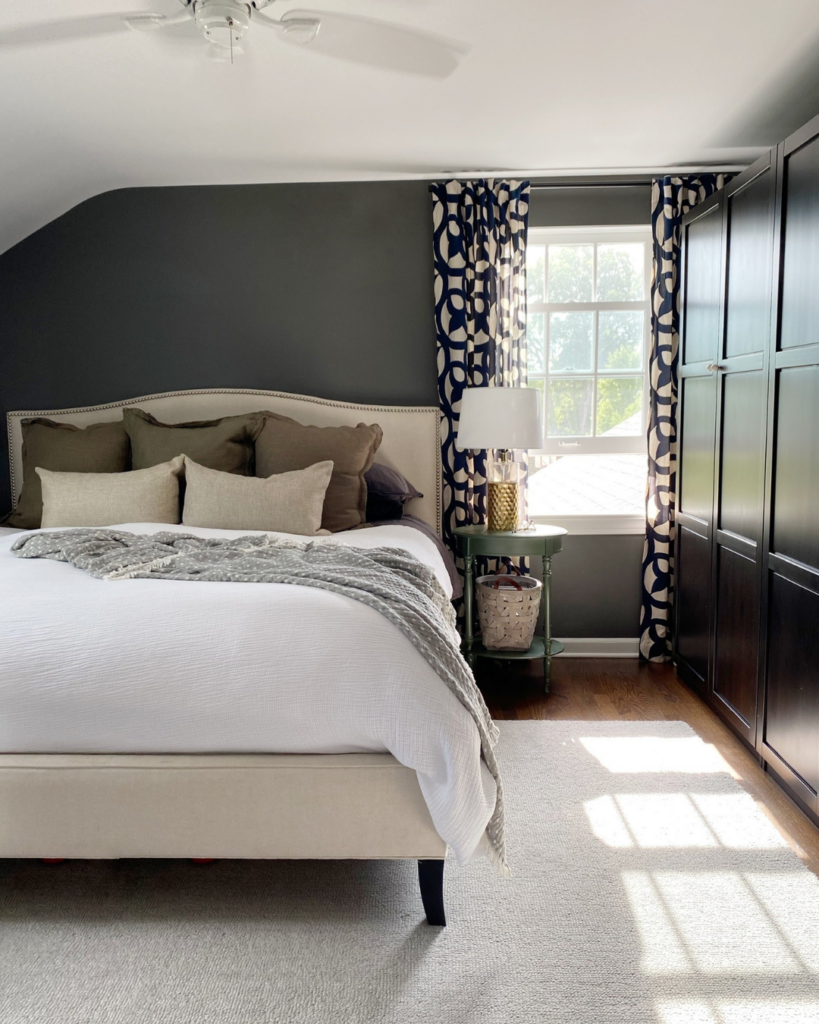 Light and airy primary bedroom with dark chocolate walls, a neatly made bed, and cleverly designed Ikea hack wardrobe cabinets.