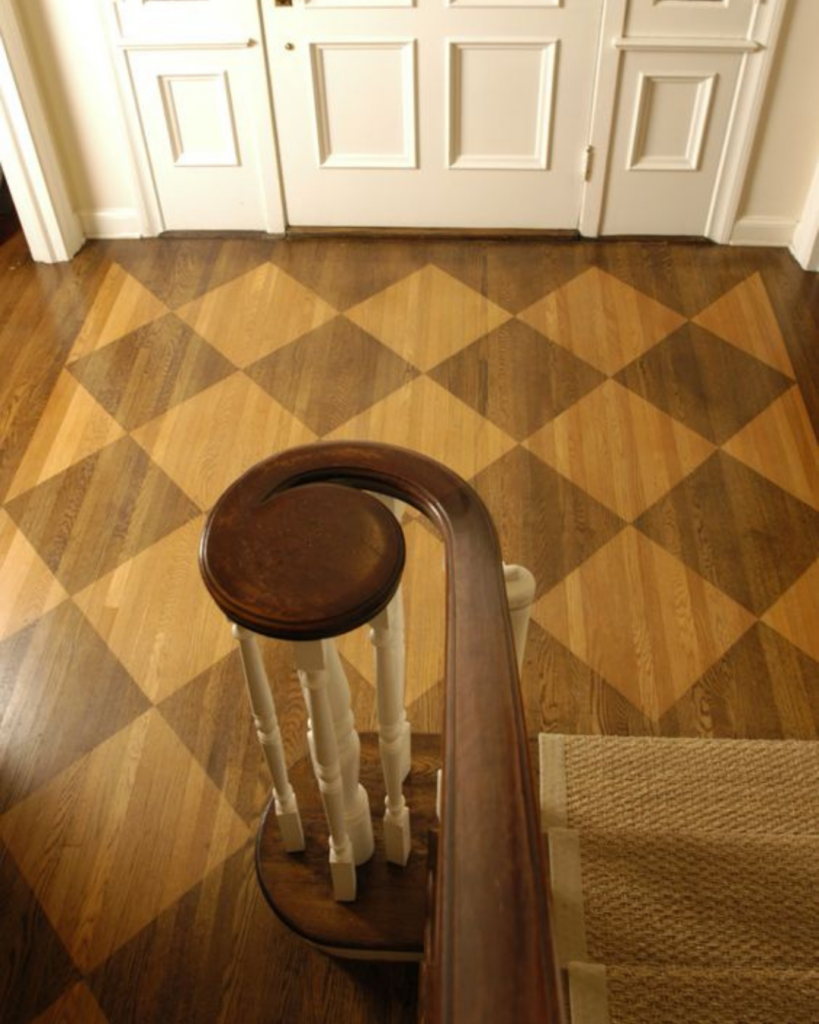 Overlooking view from a staircase showing a wood floor stained in a checkerboard pattern with a sisal stair runner, featured in MMDH HQ home project updates.